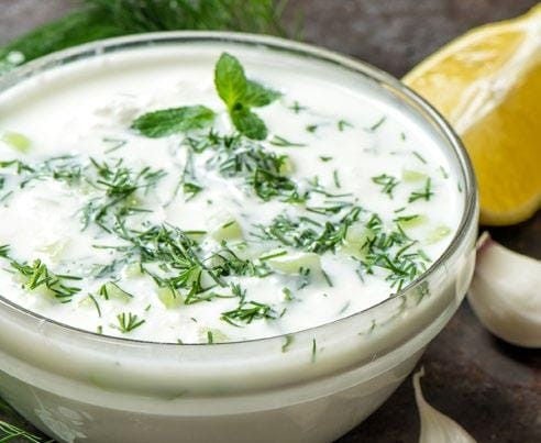 Vegetable dip in a clear glass bowl with fresh garlic cloves sitting next to it