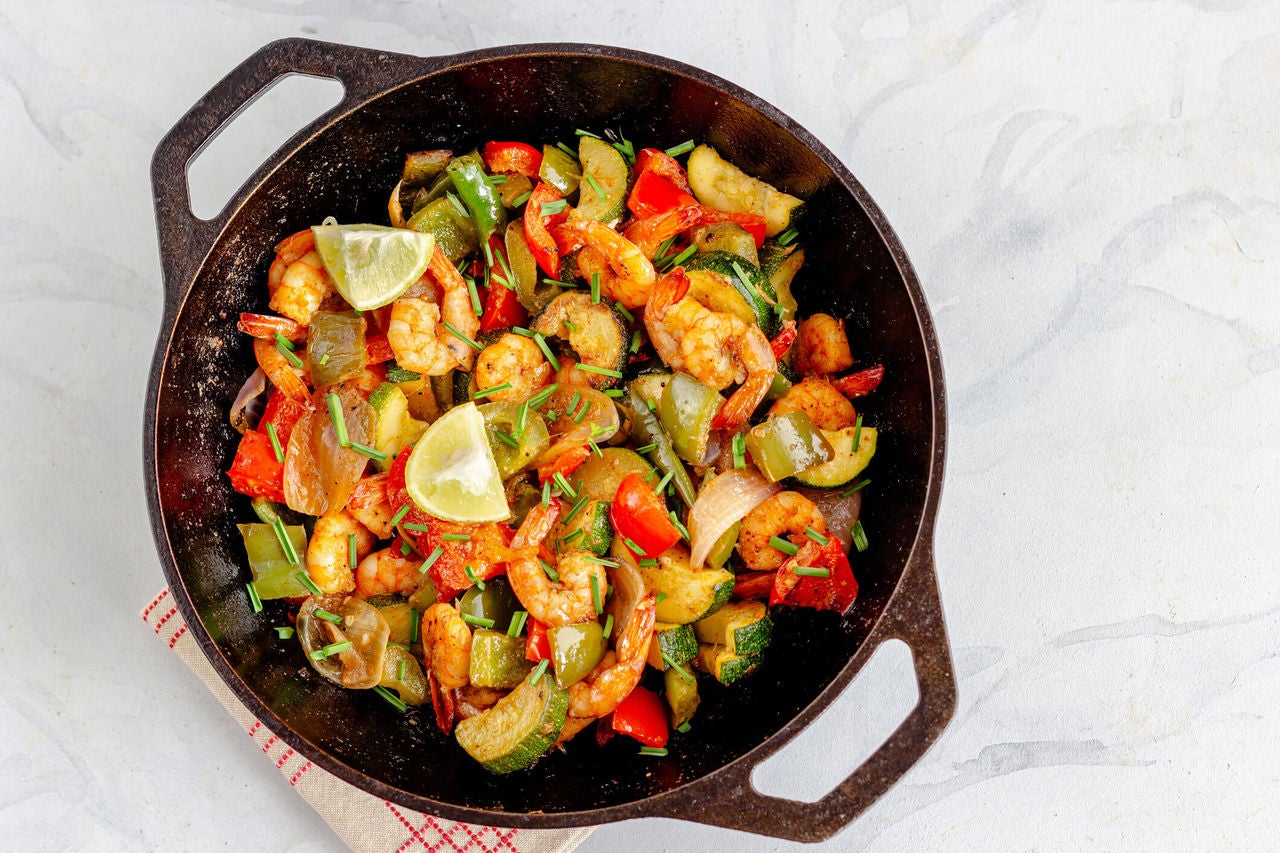 Pan with chopped veggies, seasoned shrimp, chives and lime wedges.