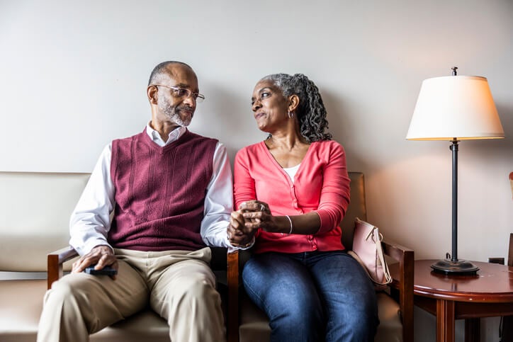 Older couple sitting in a waiting room holding hands and looking at each other while smiling.