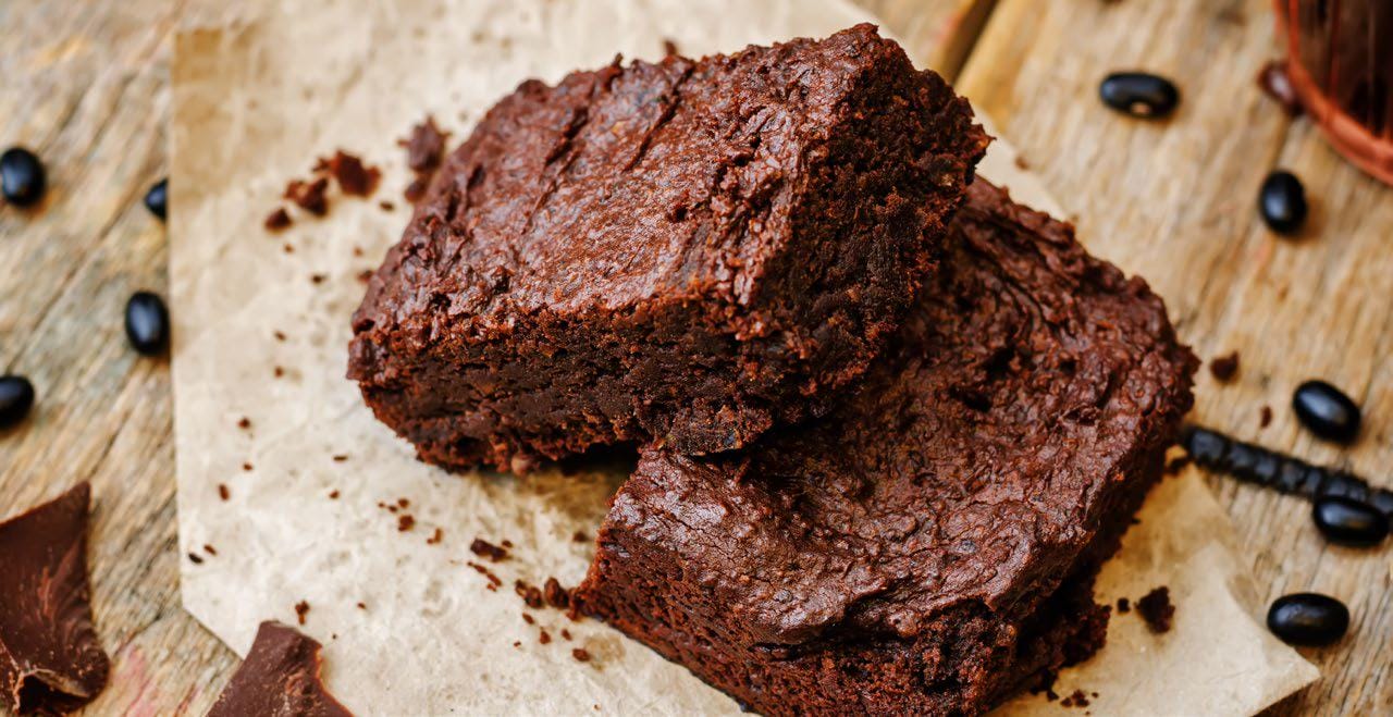Rich chocolate brownies made with black beans, stacked on parchment paper with chocolate pieces and black beans nearby.