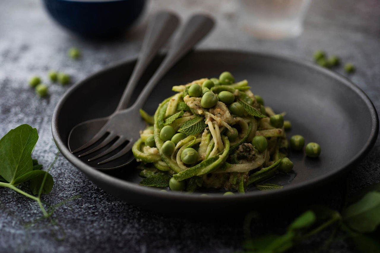Plate with pasta and zucchini pasta with pesto sauce and peas.