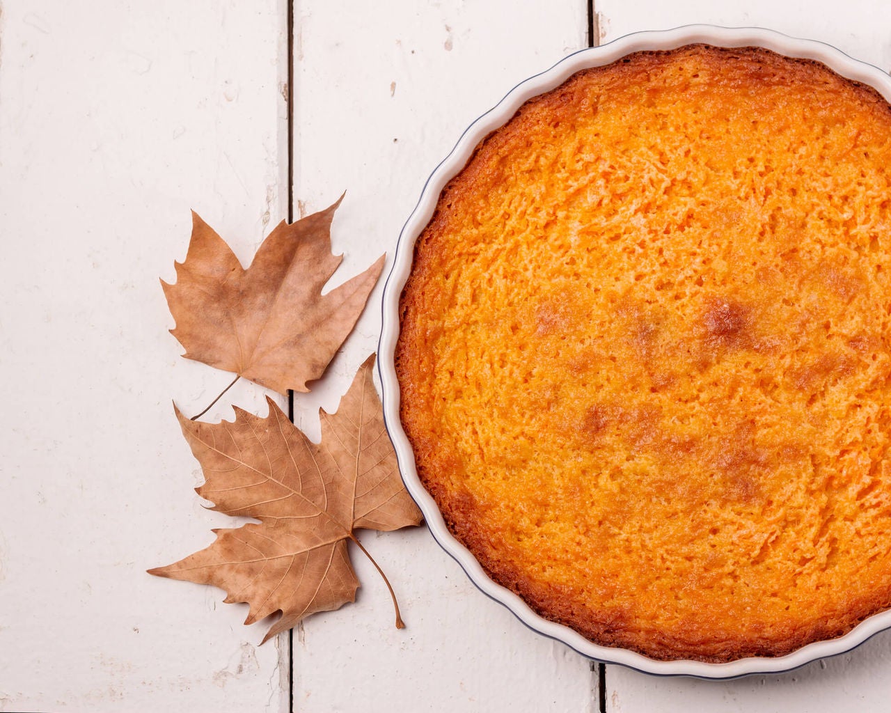 Crustless pumpkin pie in a pie dish with autumn leaves next to it. 