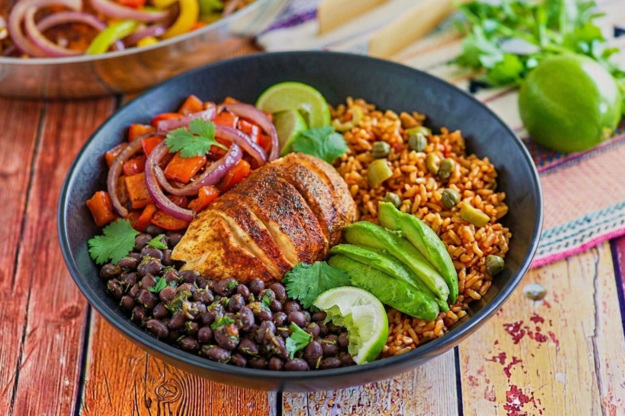 Large bowl with sliced seasoned chicken breast, black beans, peppers, onions and seasoned brown rice.