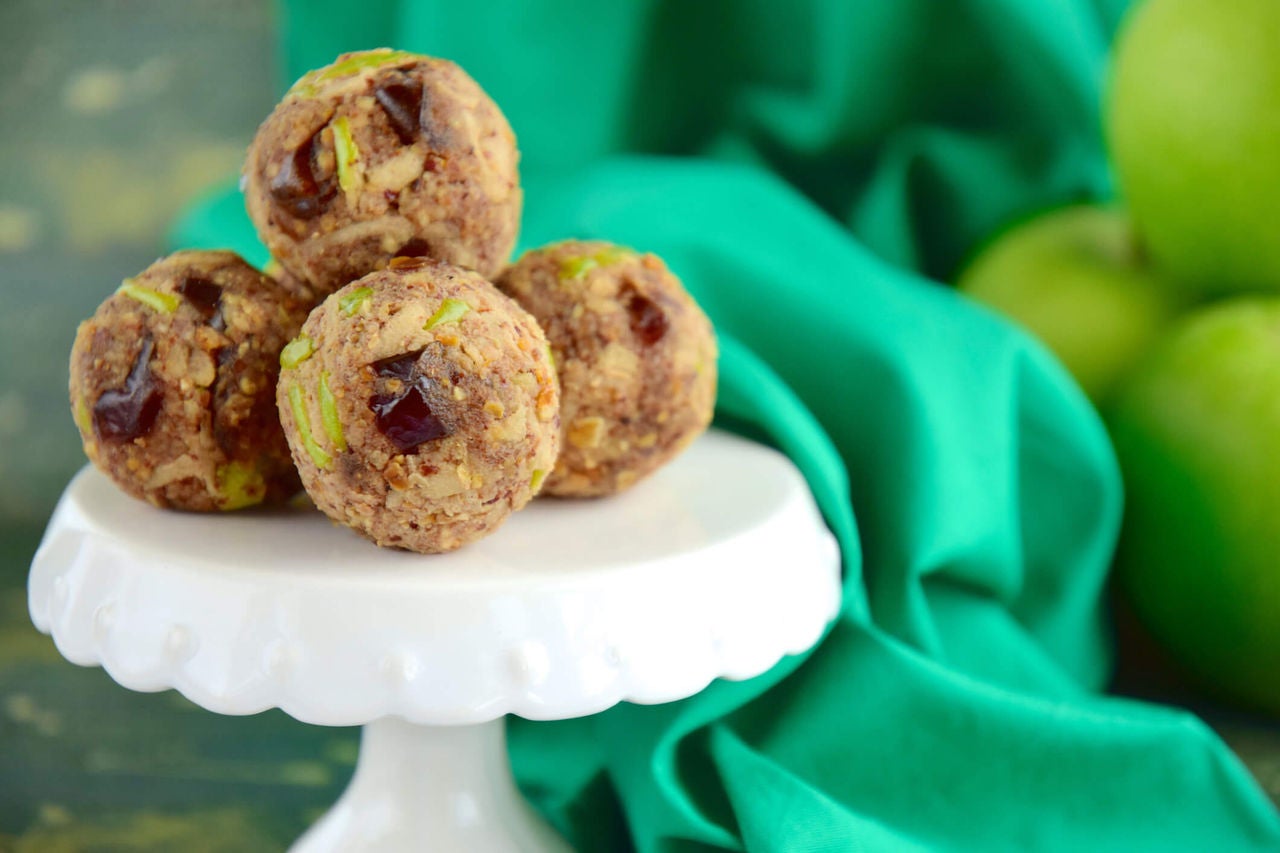 Apple oat date balls piled in a pyramid on a white cake stand.