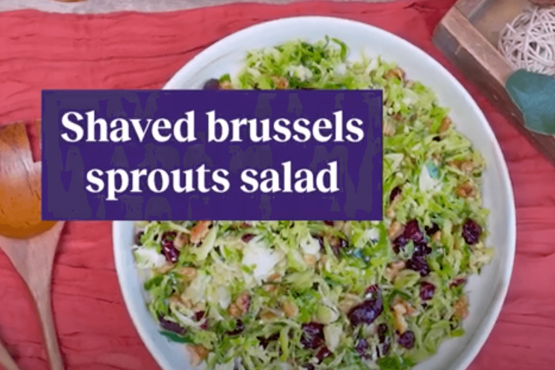 Bowl of shaved Brussels sprouts salad with wooden spoon and red tablecloth