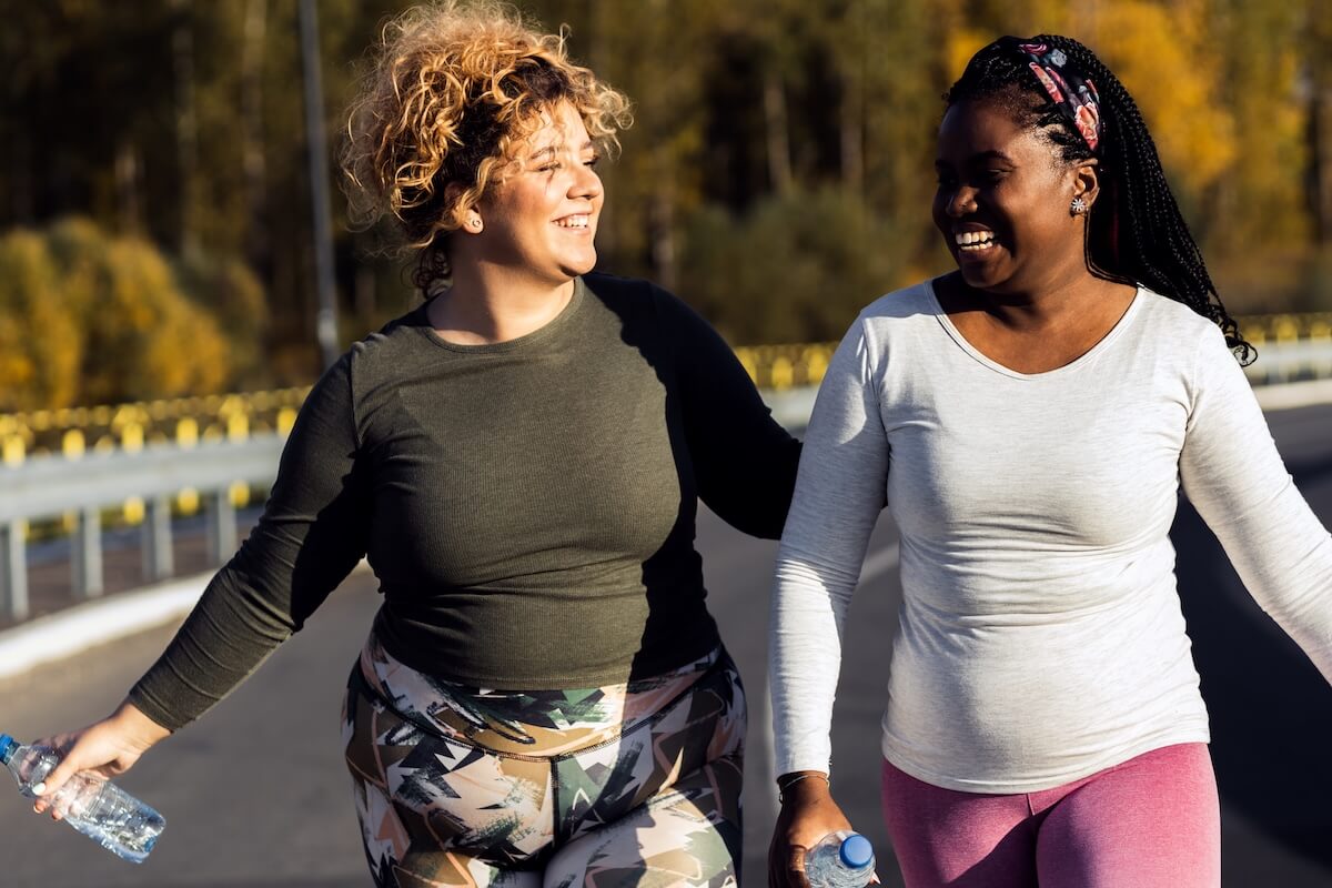 Two women wearing athletic clothing walking together on an outdoor path.