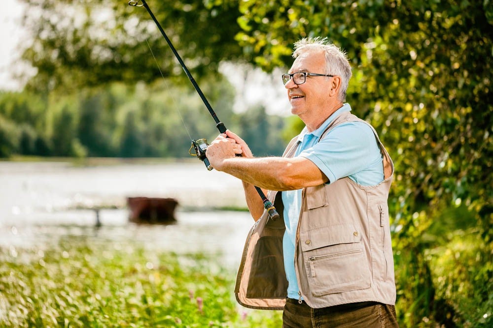 Happy senior man is fishing on sunny day. 