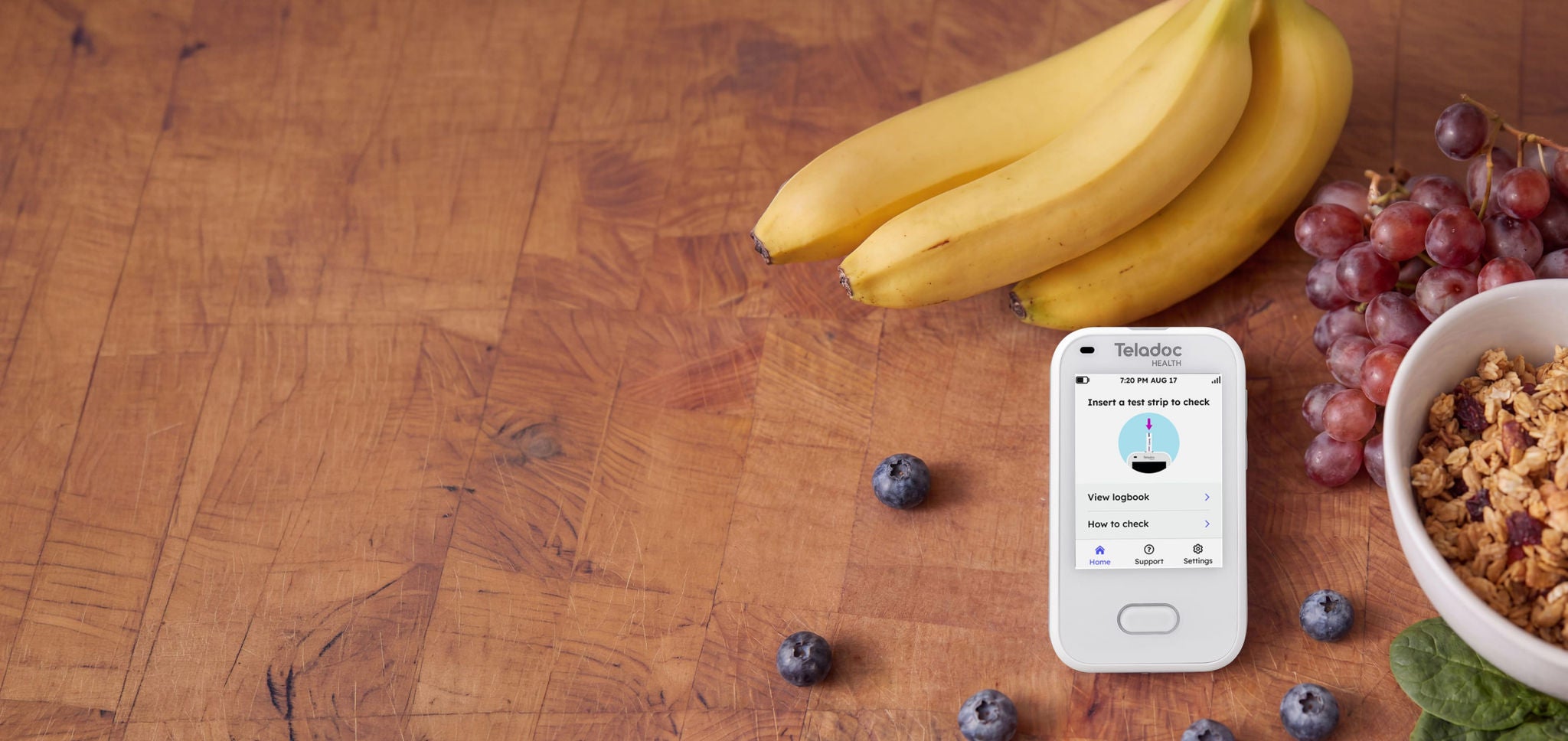 Mobile phone on a table with bananas, grapes, blueberries and a bowl with cereal in it