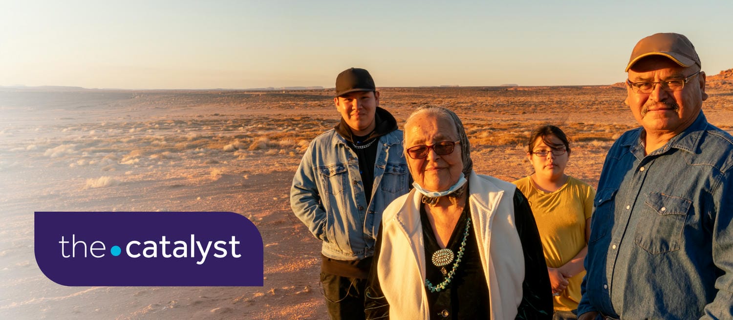Four people standing in a sunlit desert landscape at sunset, with The Catalyst logo in the upper-left corner.