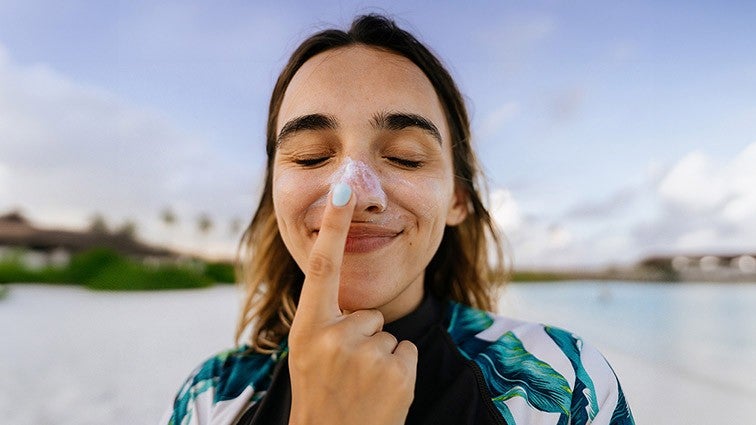 A young woman applying sunscreen to her nose while smiling playfully