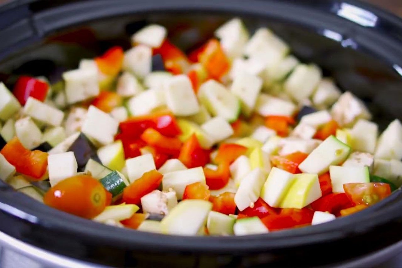 Slow cooker filled with chopped colorful vegetables including zucchini, tomatoes, and bell peppers