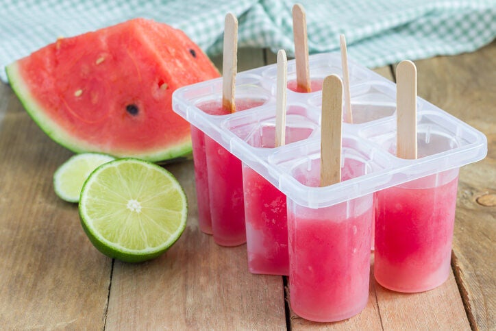 Watermelon popsicles in a popsicle mold next to sliced watermelon and limes.