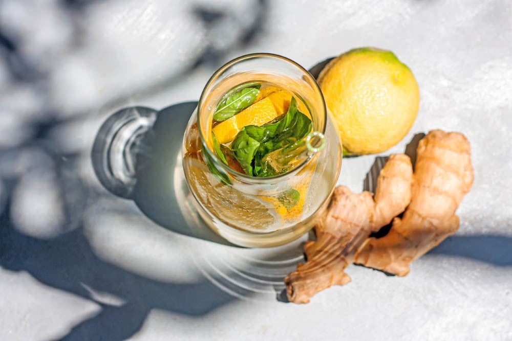 Cold refreshing summer drink or cocktail in carafe with glass straw. Detox water or lemonade with slices of lemon and basil in glass carafe with recyclable straw. Summertime zero wast concept. Selective focus.
