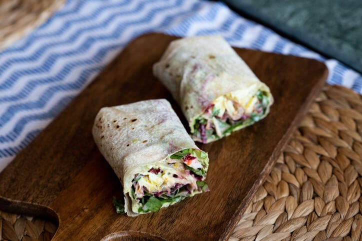 Two hummus and veggie wraps on a wooden board. 
