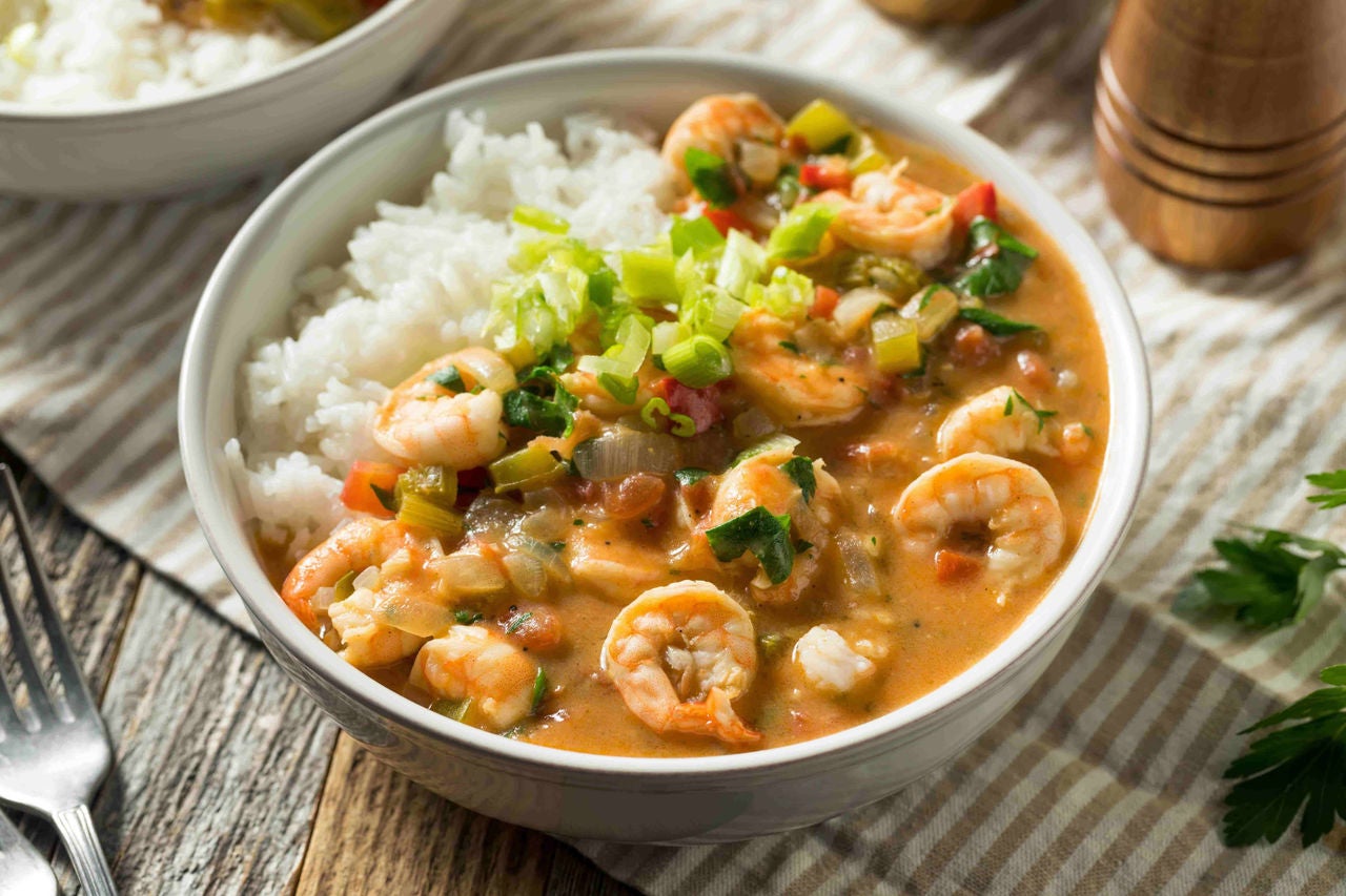 Bowl of cajun shrimp and rice on a set table with a fork and salt and pepper shakers nearby.