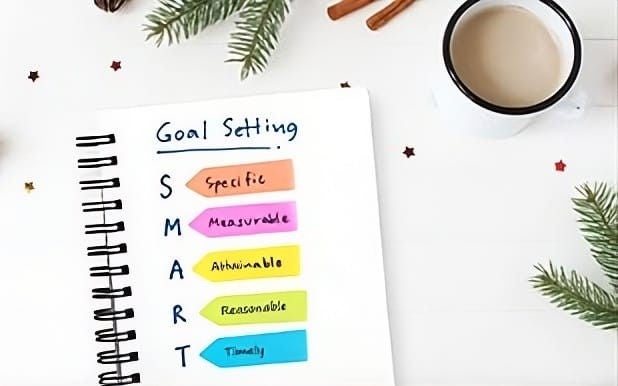 Goal setting with the SMART acronym written out on a notebook with a pencil and glasses sitting next to it