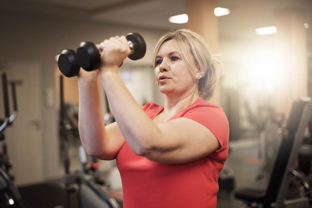 Mujer con remera roja levantando pesas en un gimnasio.