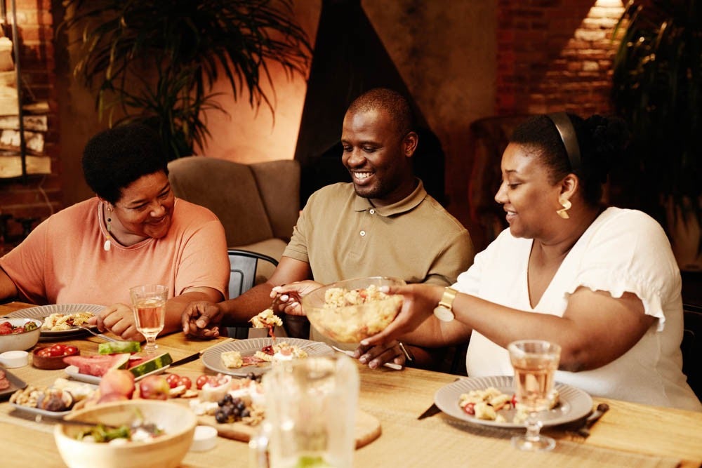 Warm toned portrait of happy African-American family sitting at table outdoors and enjoying dinner together at evening