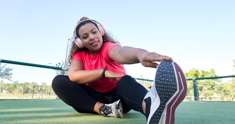 Smiling woman in sportswear stretching her leg while wearing headphones outdoors.