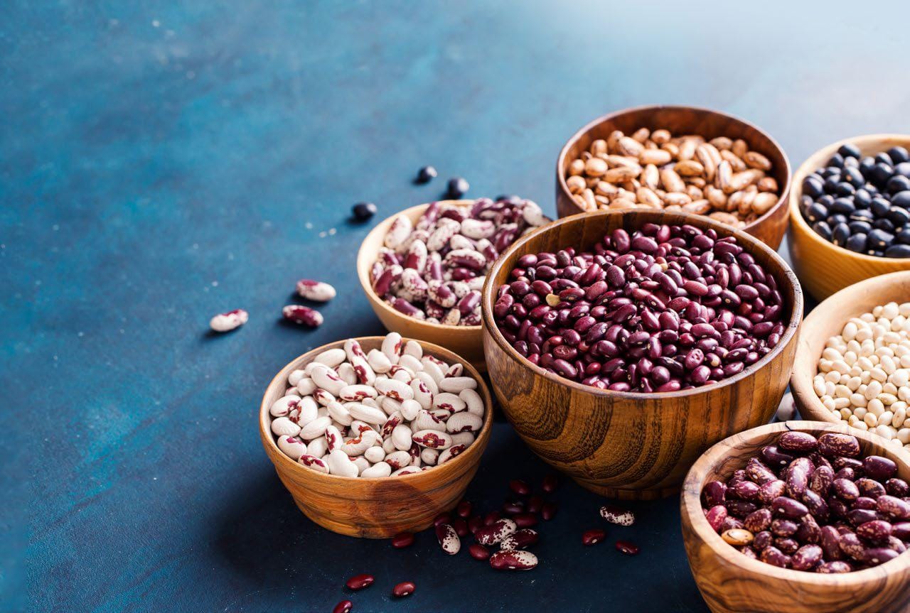 Assorted dried beans and legumes displayed in wooden bowls on a blue surface