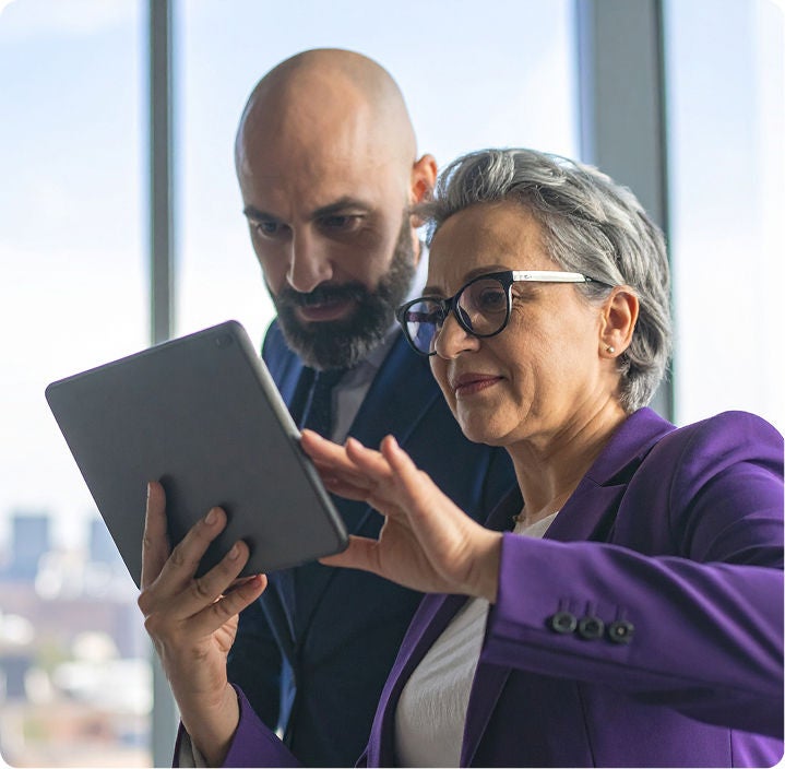 Two professionals reviewing information on a tablet in an office setting.