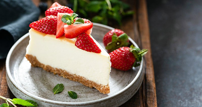 A plate with a slice of cheesecake. The cheesecake is topped and garnished with freshly sliced strawberries