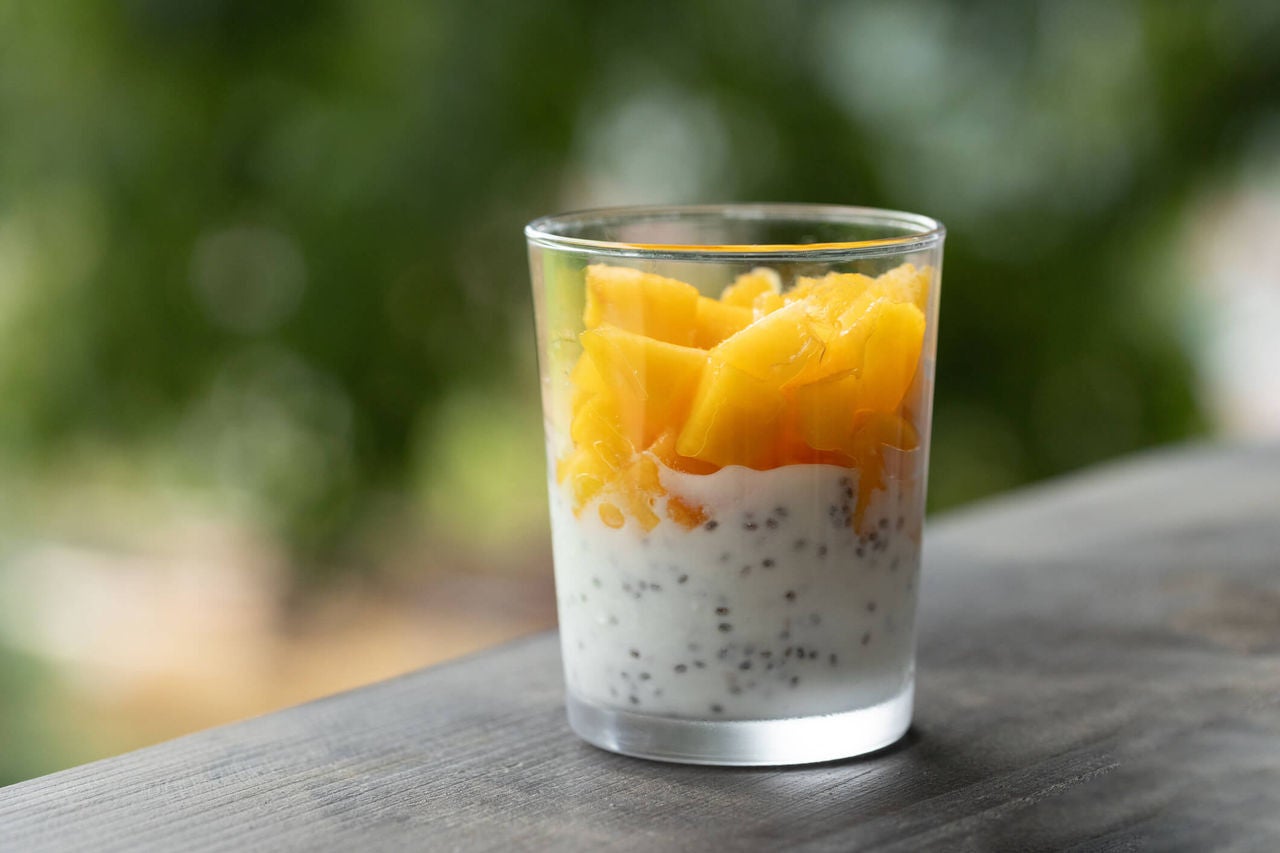 Cup with yogurt, chia seeds and chunks of papaya on an outdoor surface.