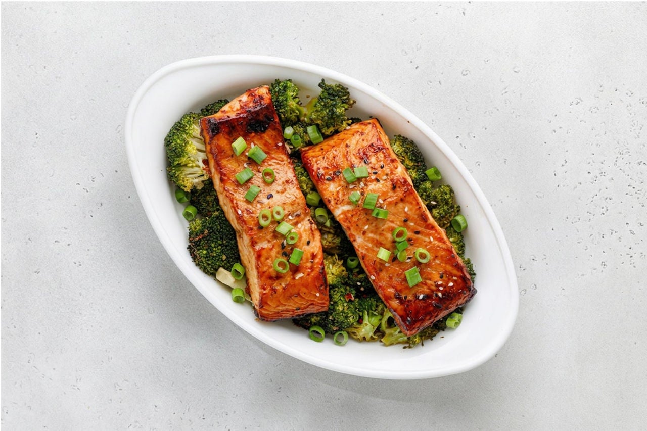 Dish with cooked broccoli and salmon topped with scallions. 