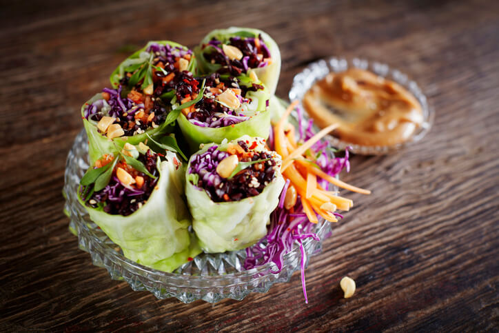 A bowl with six rice paper veggie wraps with a side of peanut dipping sauce.