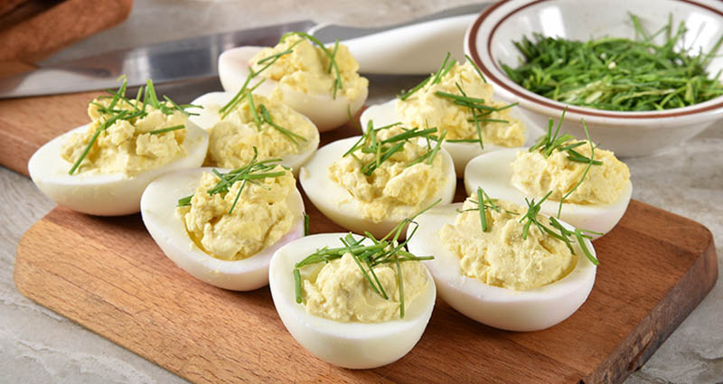 Deviled eggs served on a cutting board topped with fresh chives