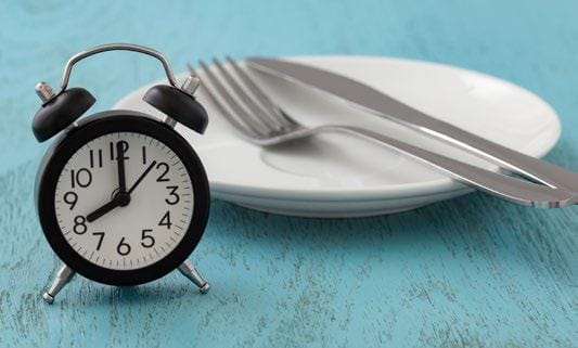 Clock in front of plate with a fork and knife on it