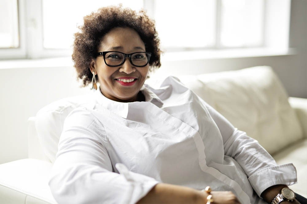 Smiling woman wearing glasses and a white shirt sitting on a white couch.