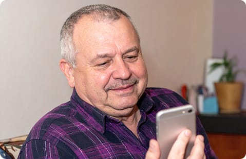 A seated man smiles while looking at his cell phone.