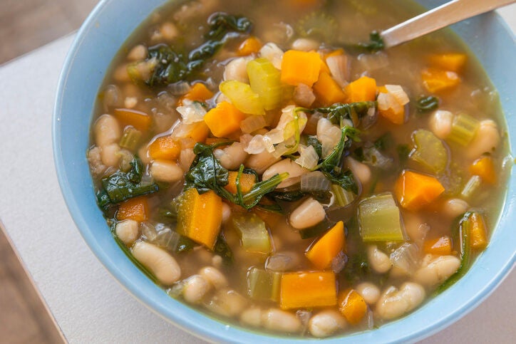 Bowl of white bean stew with chopped vegetables and greens.