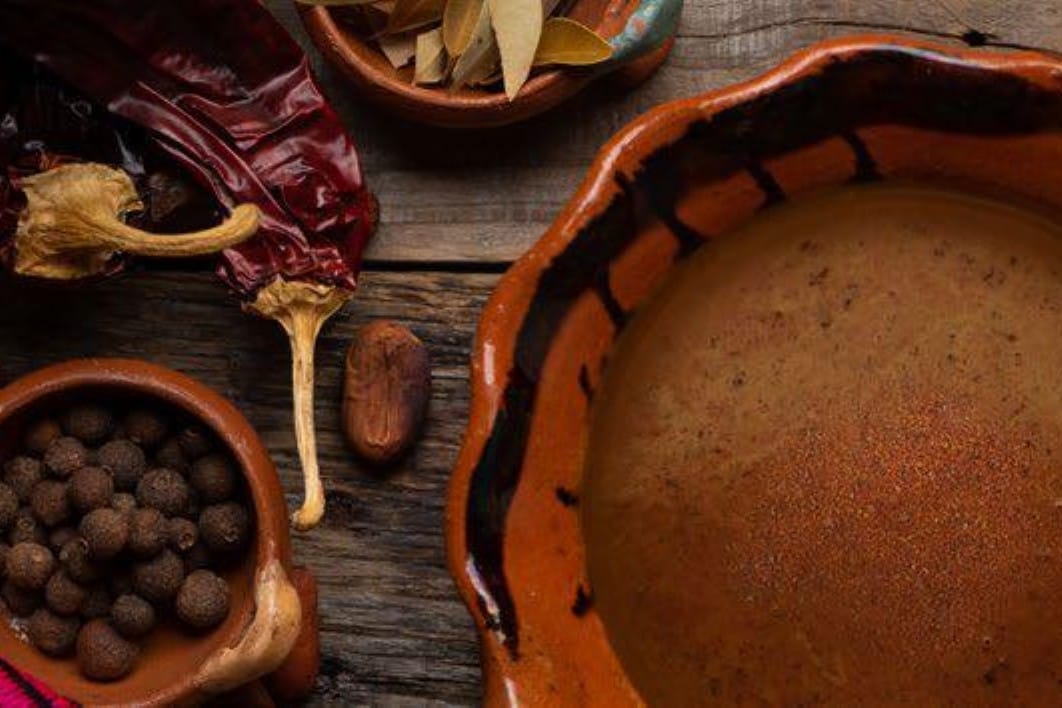 A bowl containing mole next to essential ingredients for Mexican cuisine, such as cilantro, cloves, and peppers.