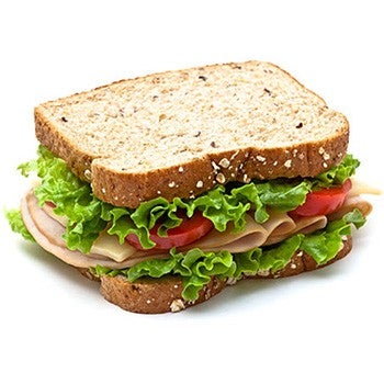 Turkey sandwich made with whole grain bread, layered with fresh lettuce, tomato slices, and cheese, isolated on a white background