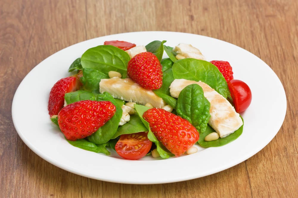 "Spinach, grilled chicken, strawberry, cherry tomatoes and pine nuts salad on white plate"