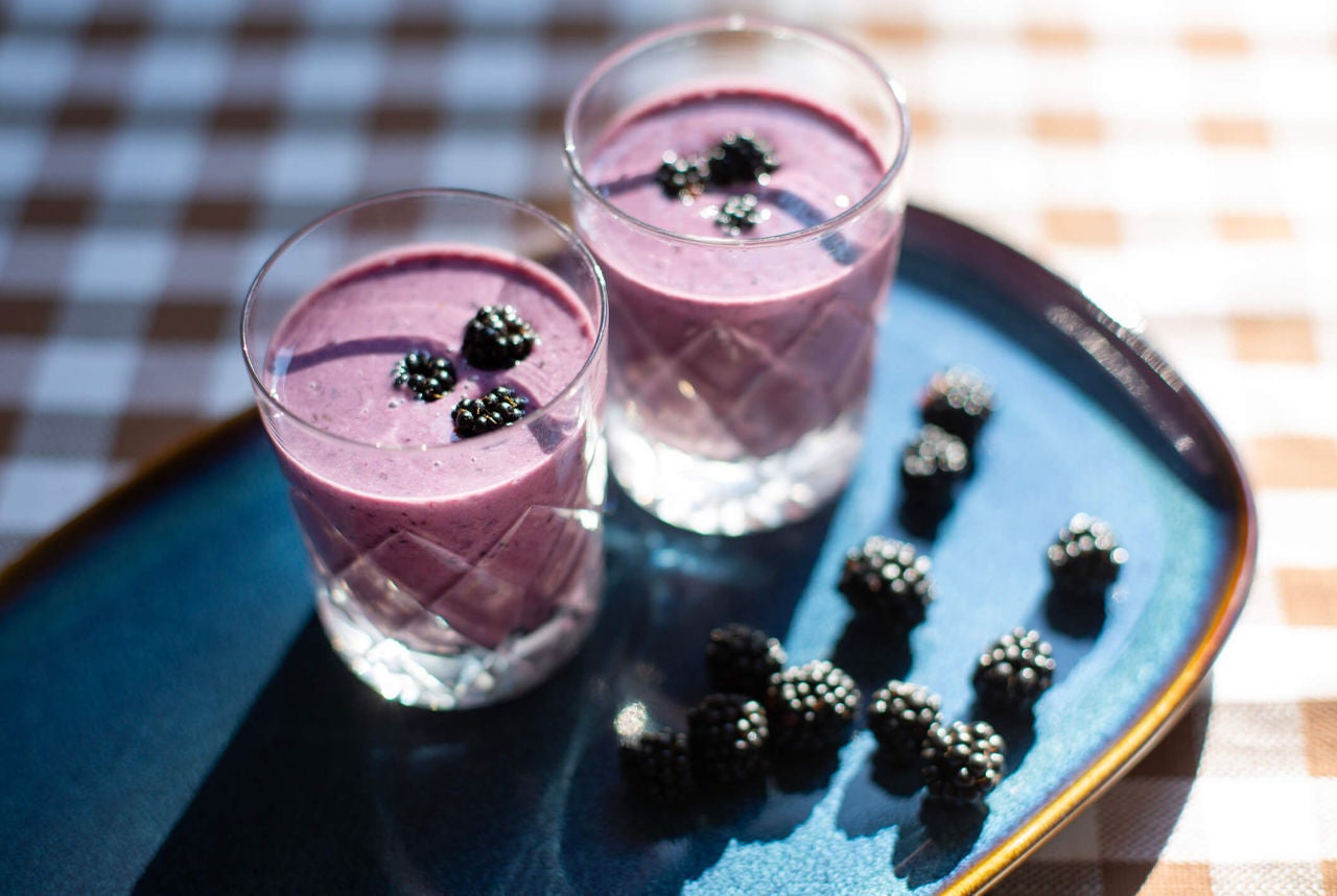 Two glasses of purple smoothie with blackberries on top as garnish.