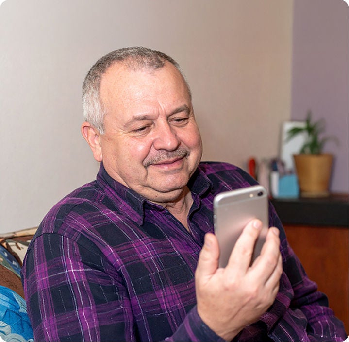 A seated man smiles while looking at his cell phone.