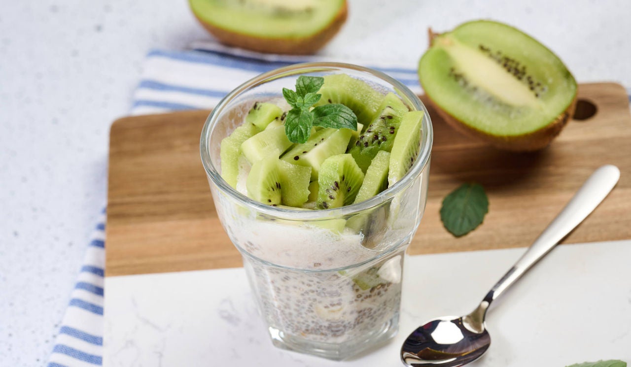 Cup with yogurt, chia seeds and sliced kiwi garnished with mint.