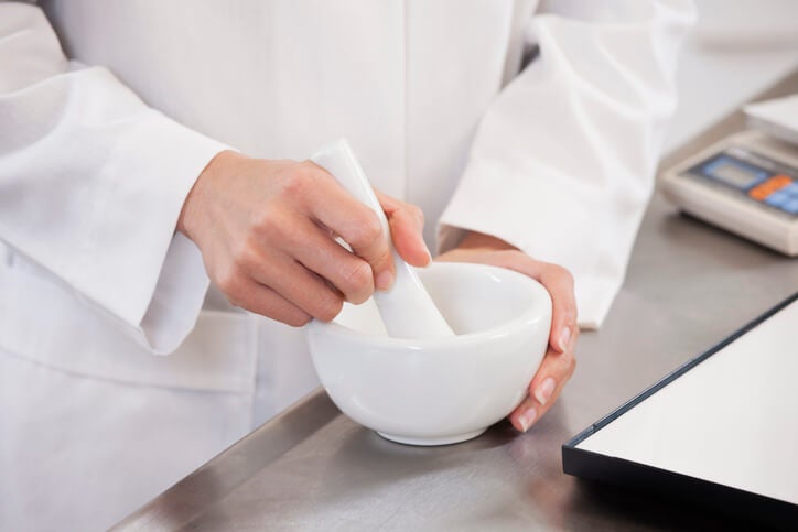 Doctor wearing a white lab coat using a mortar and pestle in a medical setting. 