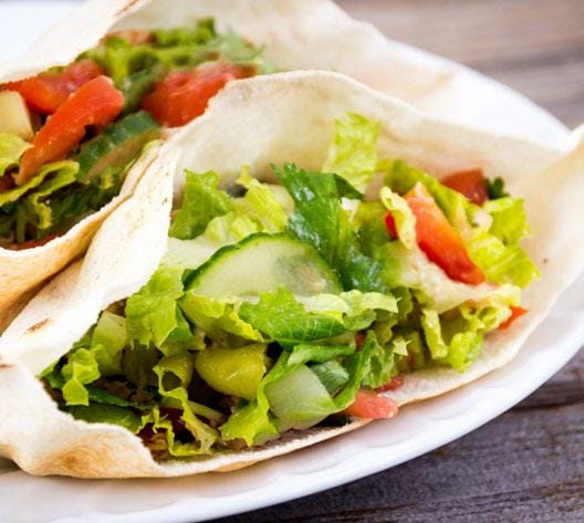 A veggie pita pocket with hummus on a plate