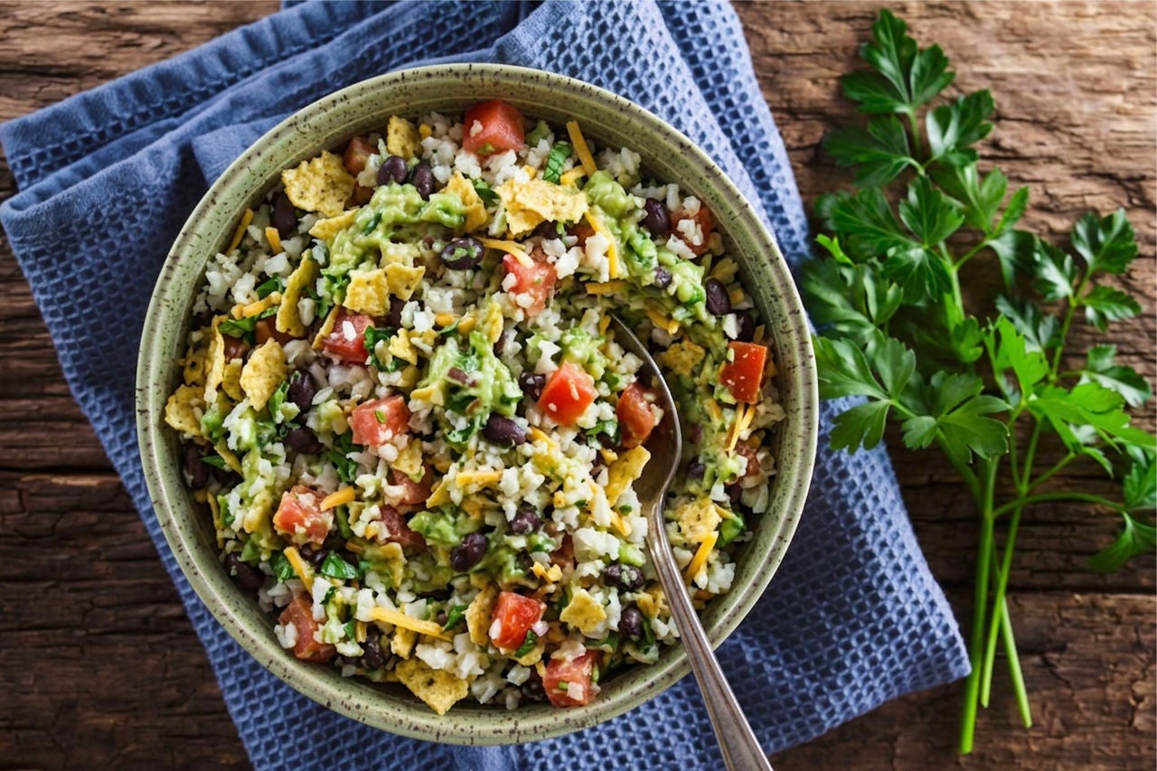 Bowl with a mixture of cauliflower rice, black beans, shredded cheese, tomato and guacamole.