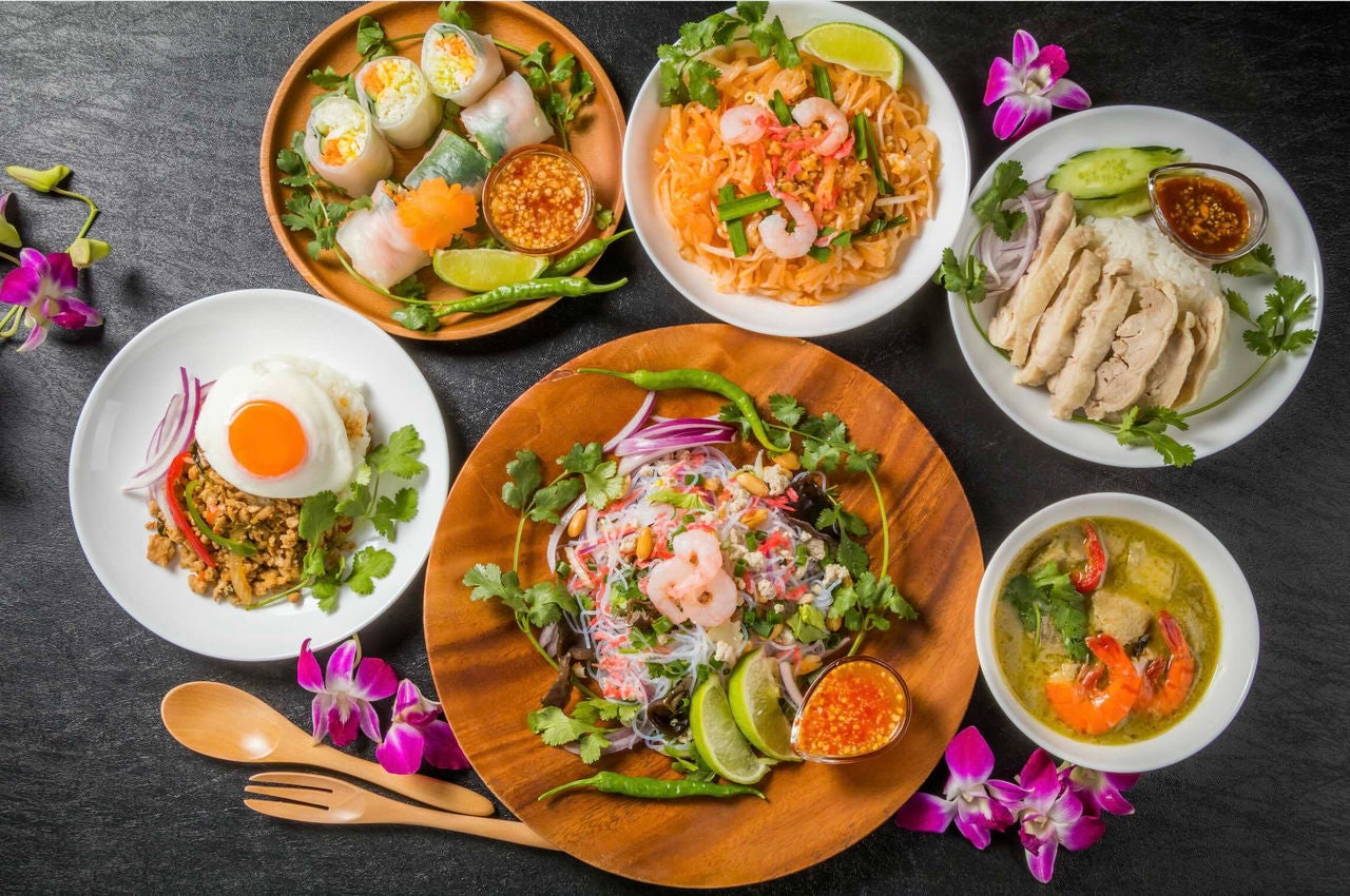 Overhead view of a table with various types of Southeast Asian dishes, garnished with pink flowers.