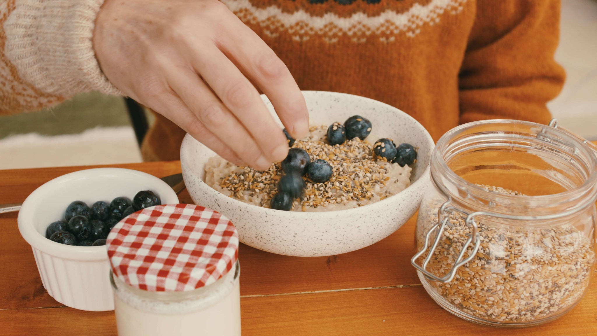 Hands sprinkling blueberries into a bowl with yogurt and flax seeds.