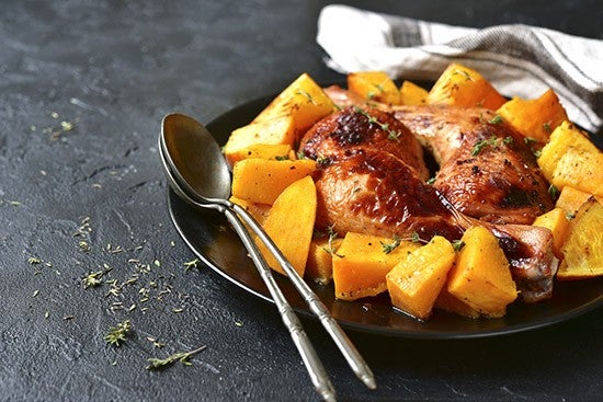Chicken legs baked with pumpkin and orange on a black plate on a stone,concrete or slate background.