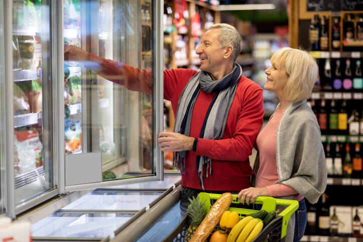 Man and woman grocery shopping, reaching into a freezer.