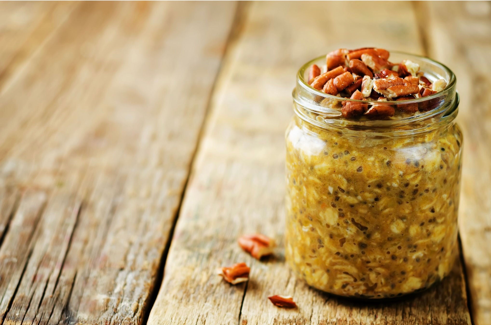 Mason jar with pumpkin overnight oats with chia seeds, topped with pecans.