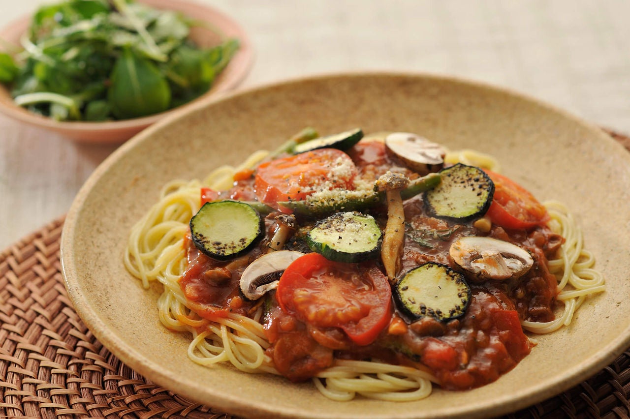 Plate with spaghetti pasta, red sauce and sliced zucchini, mushrooms and tomatoes.