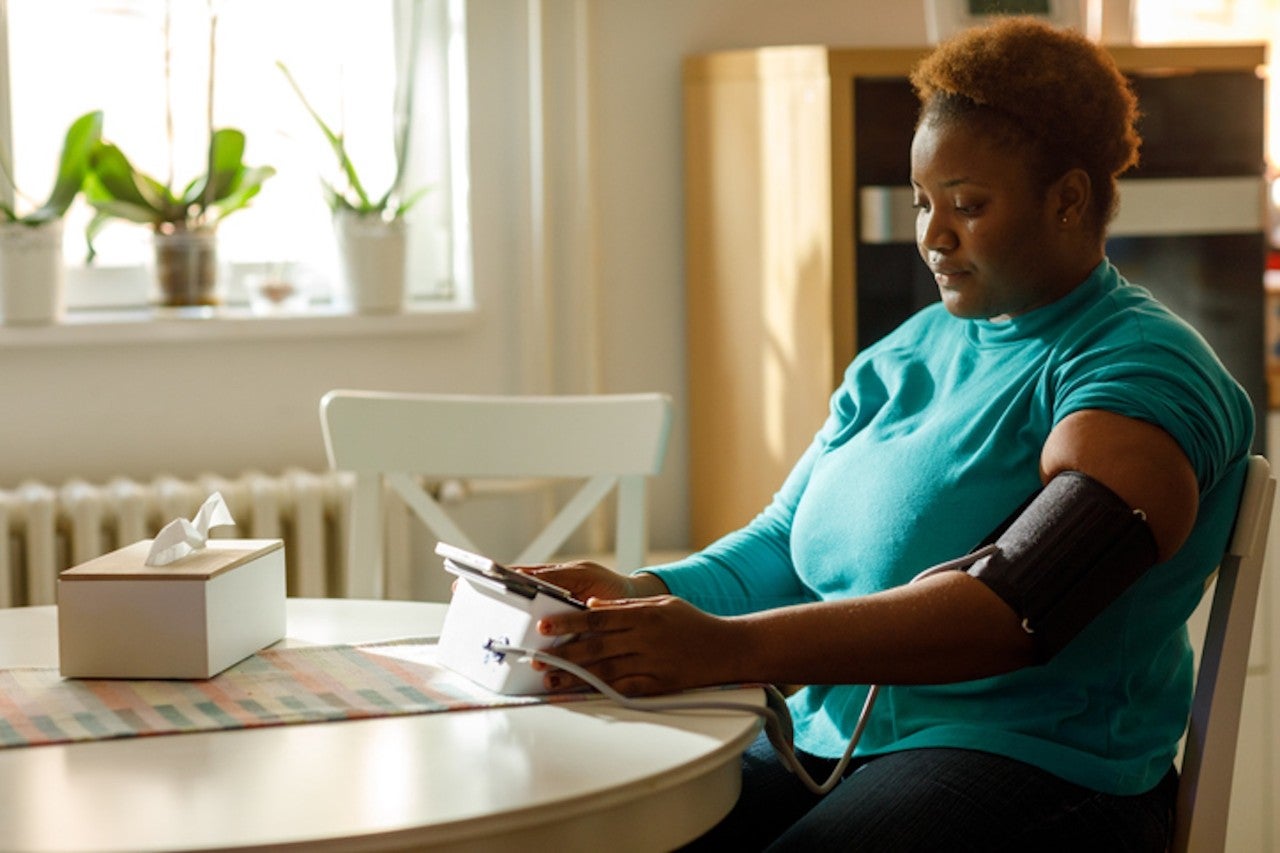 Young black woman checks her blood pressure at home.